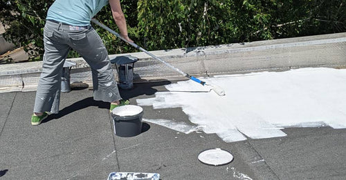 Homme sur le toit d'une maison qui pratique le cool roof avec son rouleau méché